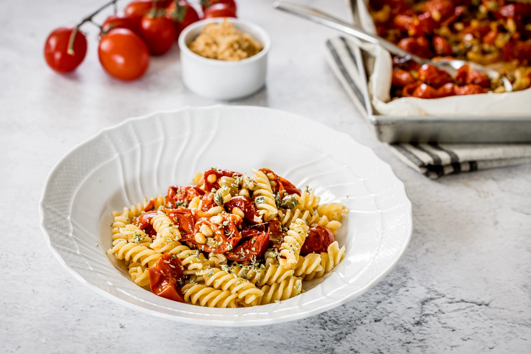 Fusilli con pomodorini, pinoli, uvetta e capperi in un piatto bianco