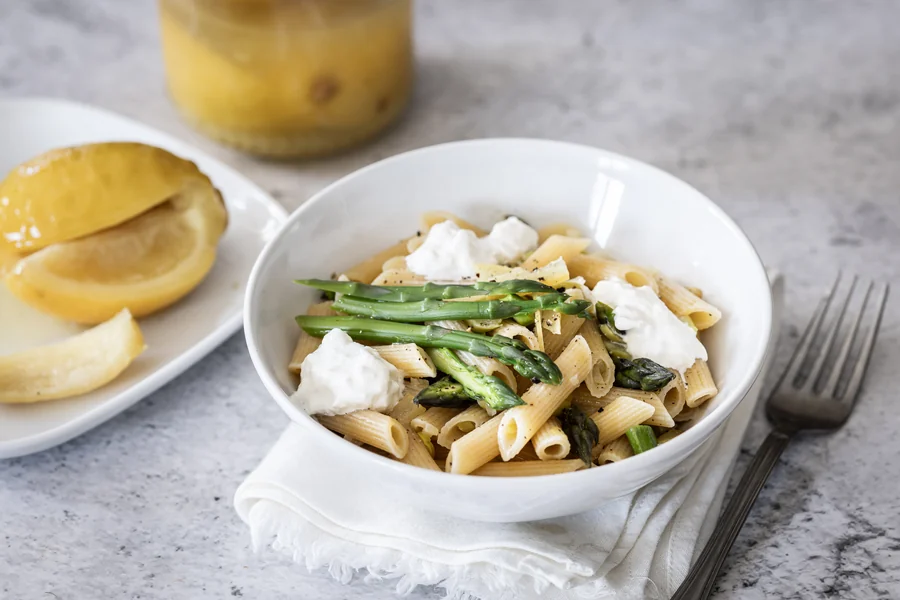 Ciotola di penne con asparagi e burrata, con limoni confit sullo sfondo