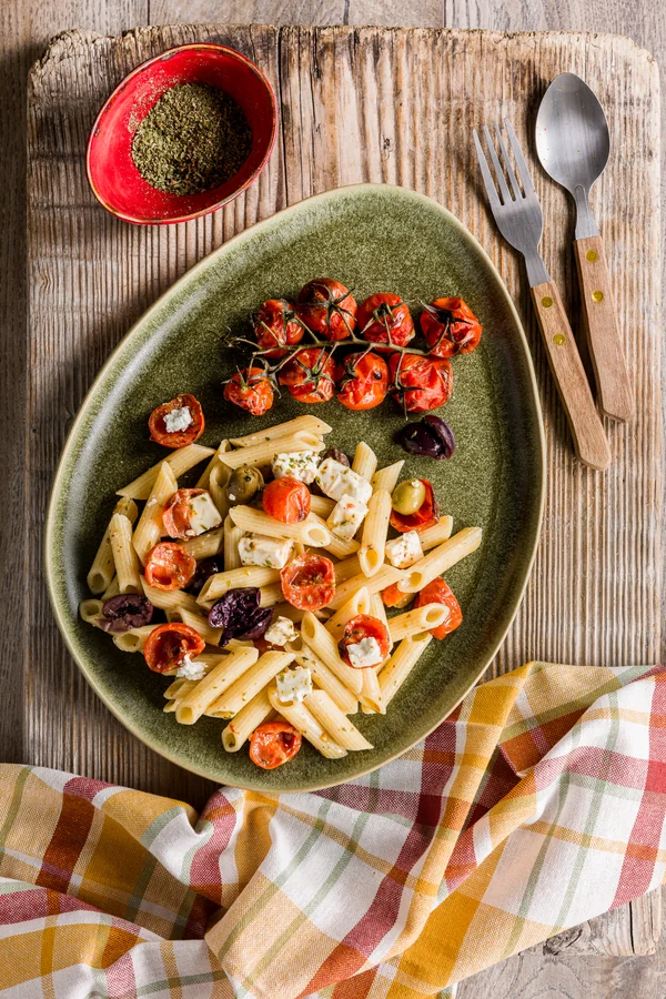 Piatto verde con penne, feta e pomodori arrosto su un tavolo di legno