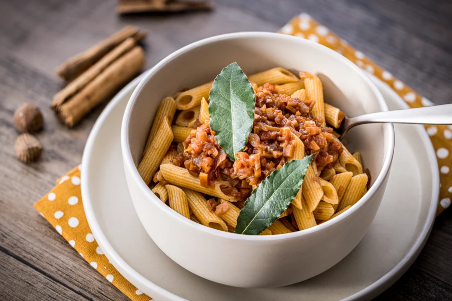 Ciotola di penne al sugo finto, con bastoncini di cannella sul tavolo